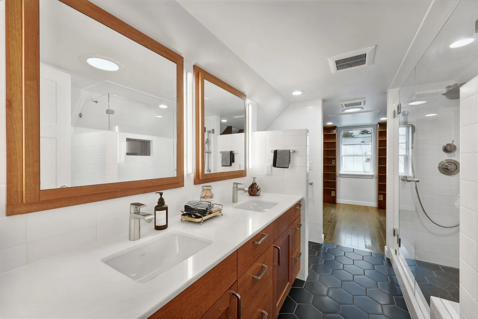 Comfortable bathroom design with double vanity, tiled shower, and warm wood details