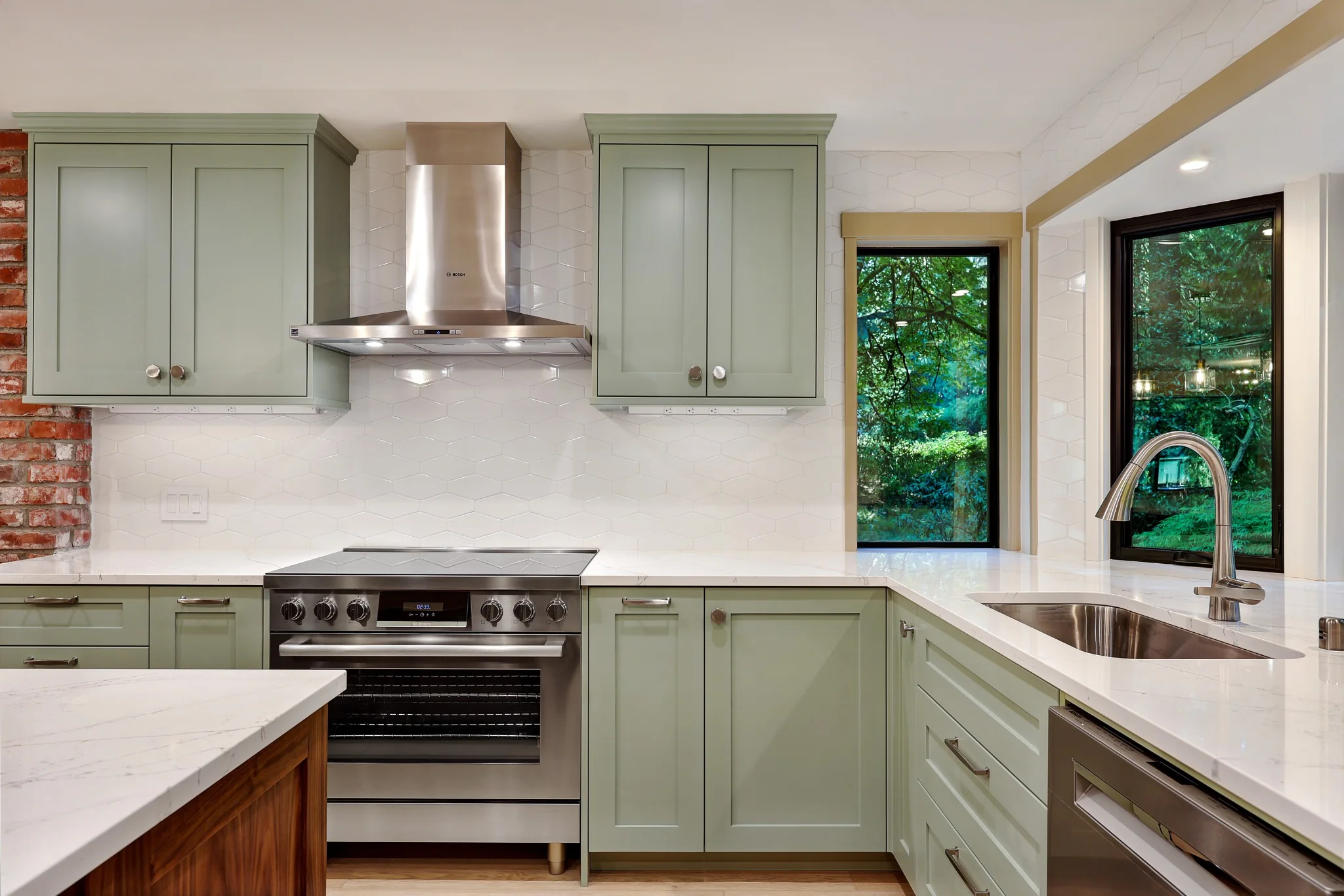 Kitchen range wall with sage green cabinets, tile backsplash, and window