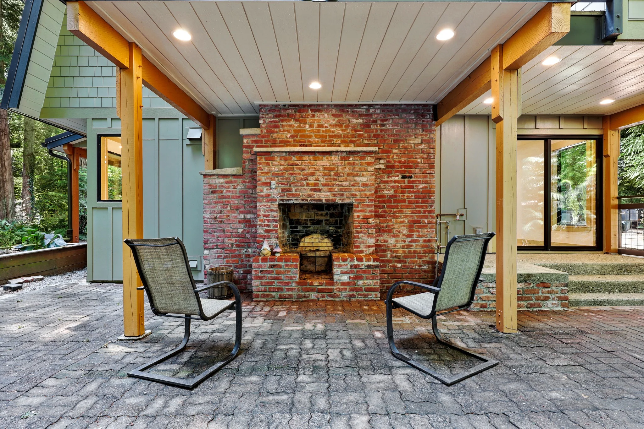 Covered patio with brick fireplace, wood posts, and paved floor